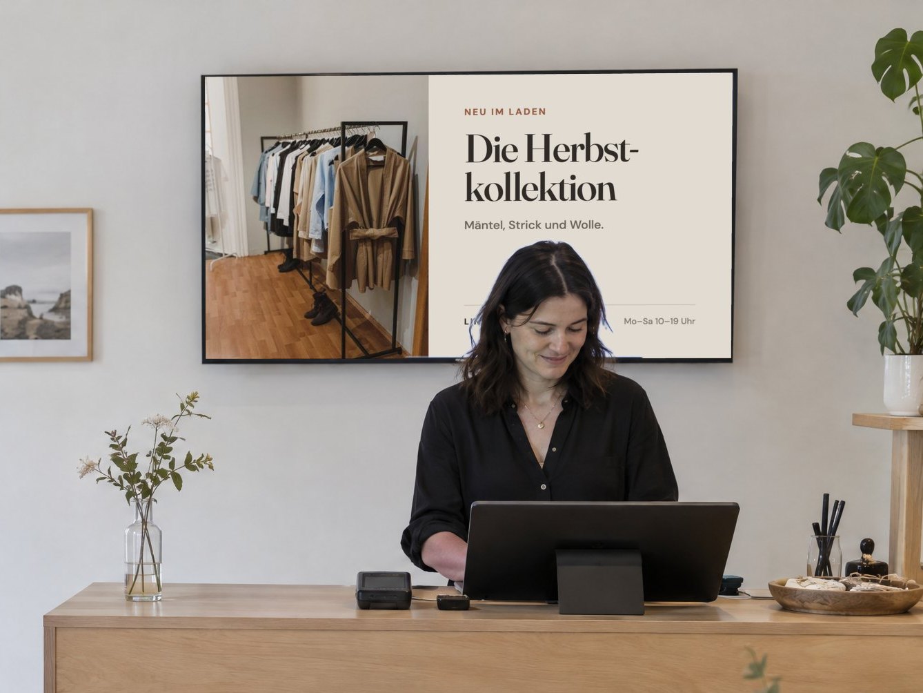 Modegeschäft, an der Wand hinter der Kasse zeigt ein Fernseher die neue Herbstkollektion.