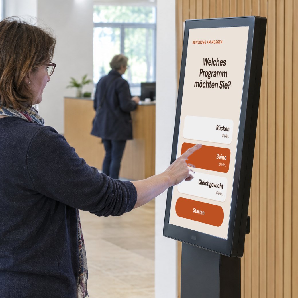 Eine Besucherin wählt am Touchscreen des digitalen Trainers ein Bewegungsprogramm.